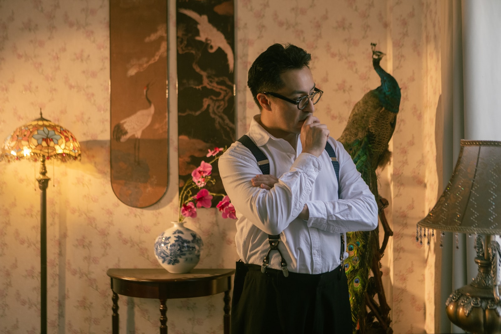 Andres in a contemplative pose, surrounded by a Chinese crane panel, peacock, Tiffany lamp, and orchids