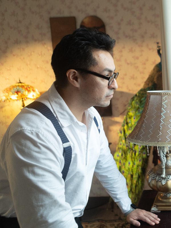 Andres Martinez at his studio, lit by a Tiffany lamp with a peacock backdrop